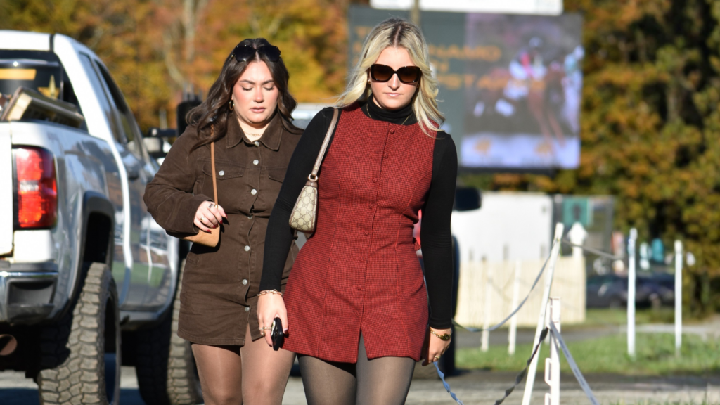 Two women in coordinated brown and red fall outfits with boots and tights at the Far Hills Race Meeting.